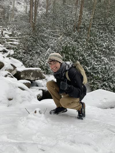 The website author in the Tennessee mountains which are covered in snow. Next to the author there is a very small snow person.